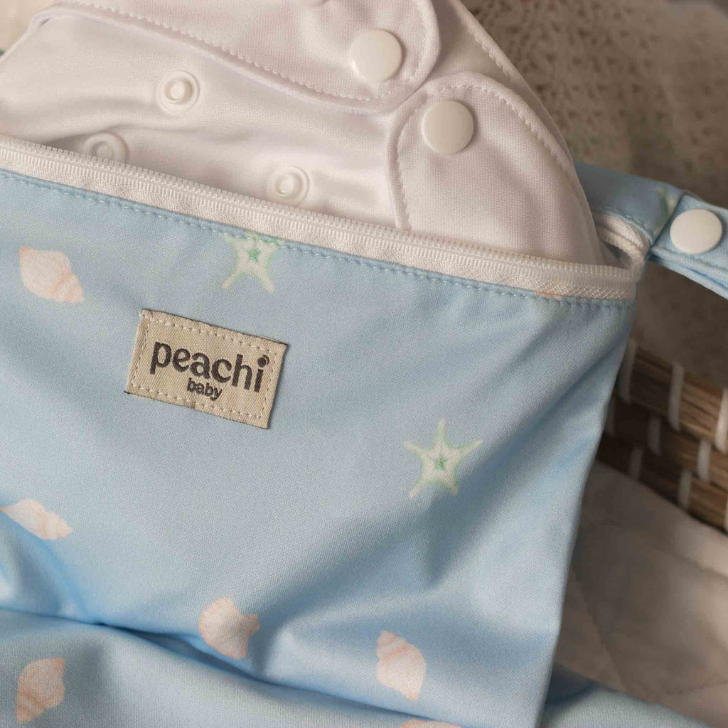 Peachi Baby Reusable Nappy Wet Bag in a Blue Seashells Print with a white cloth nappy