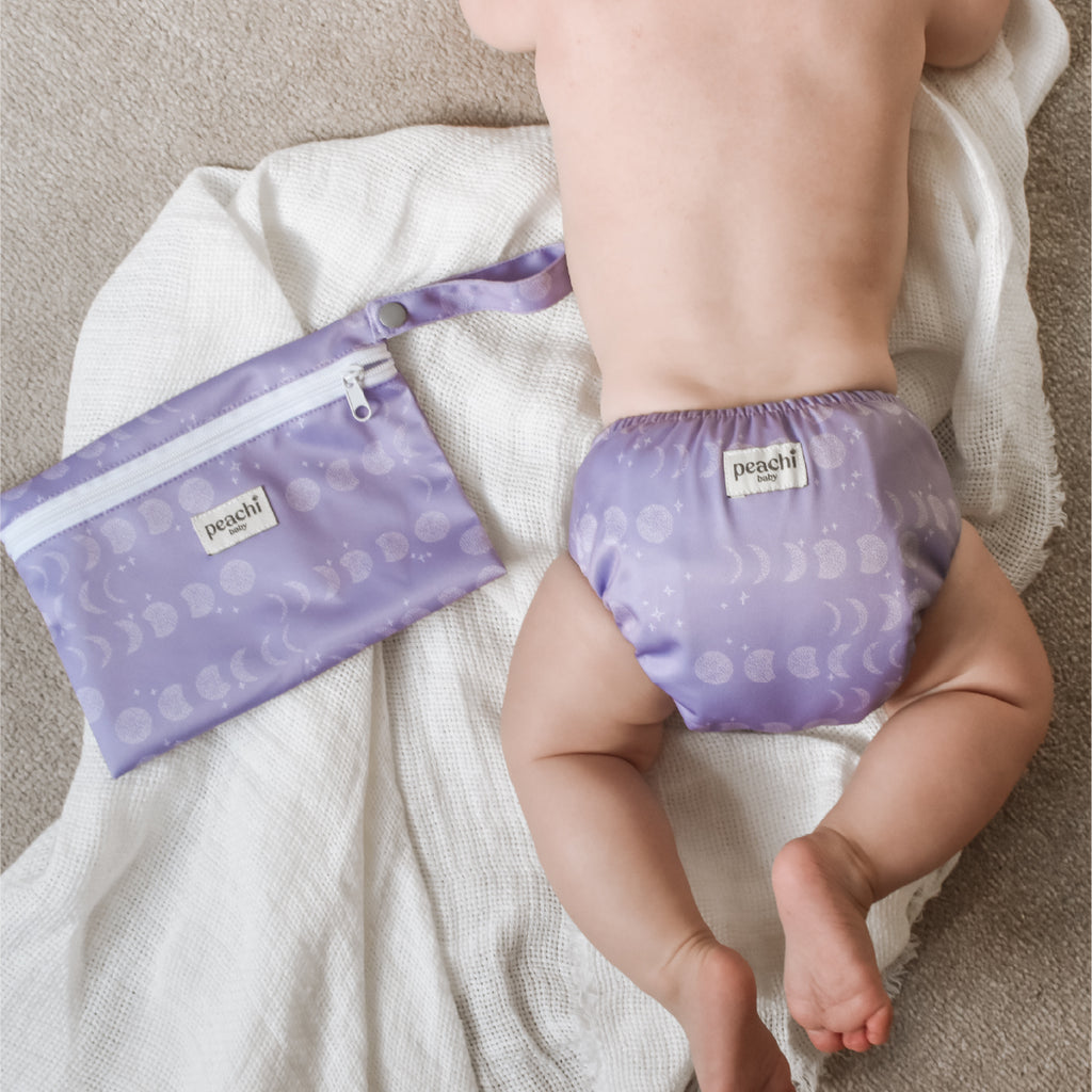 Baby wearing a reusable Nappy in a Luna Lavender print Reusable Nappy Set. Pictured alongside a matching wetbag