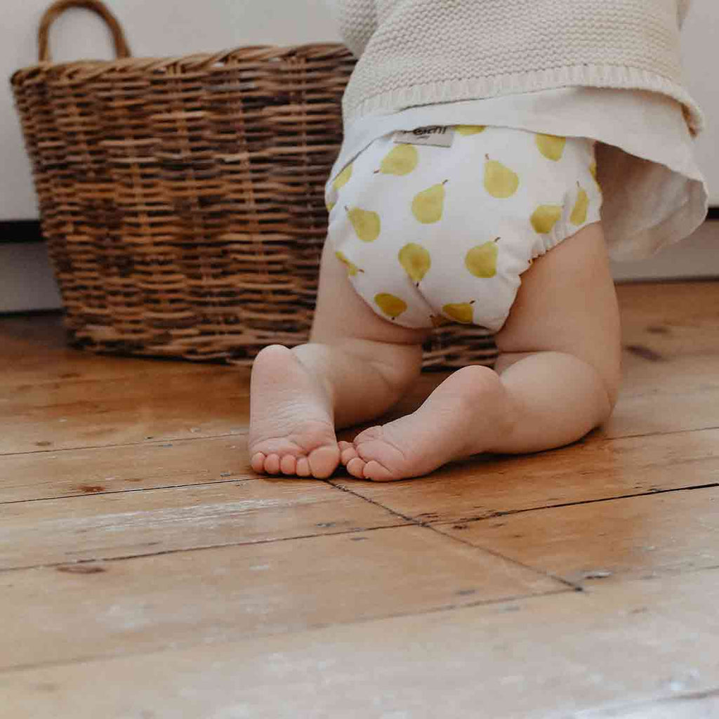 A toddler washing reusable nappies wearing a pear print modern cloth nappy by peachi baby