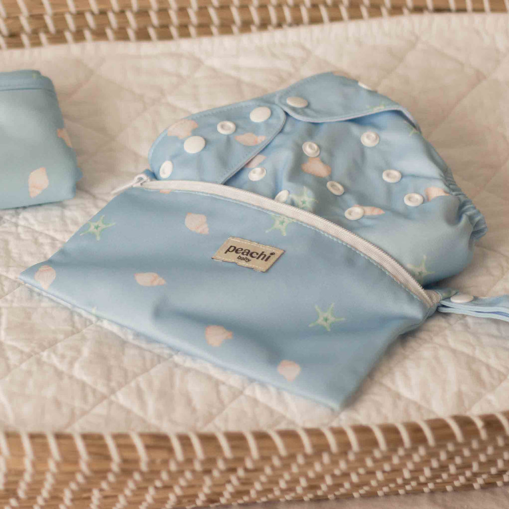 Peachi Baby Reusable Nappy Wet Bag in a Blue Seashells Print with a seashells cloth nappy on a changing mat