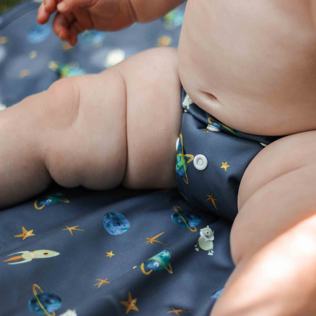 Baby wearing a Space Reusable Nappy sitting on a Space Print Space Travel Changing Mat